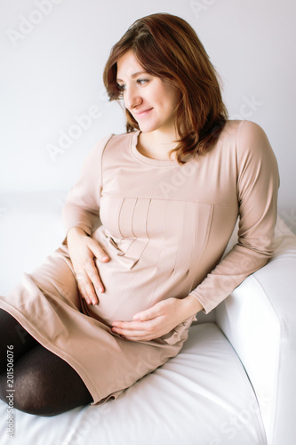 pregnancy, harmony, relaxation concept. on the comfort white sofa there is a young adorable woman that is eight months pregnant, she is expecting happy mother