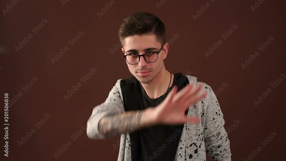 A cheerful modern man in hipster clothes stands in the Studio on a brown background and spends in front of his face with his hands. A cheerful modern man in hipster clothes stands in the Studio on a brown background and spends in front of his face with his hands.