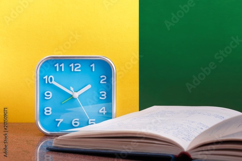 Blue alarm clock and opened personal organizer on yellow and green background