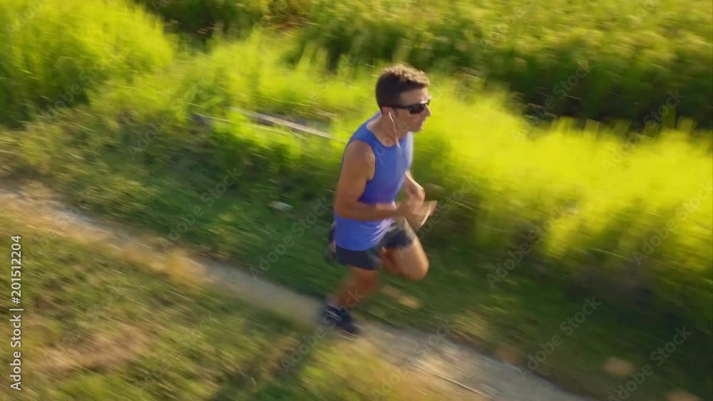 Aerial tracking backwards on young sport runner man in off road running workout at a beautiful grass field landscape in healthy lifestyle body care and fitness concept Aerial tracking backwards on young sport runner man in off road running workout at a beautiful grass field landscape in healthy lifestyle body care and fitness concept