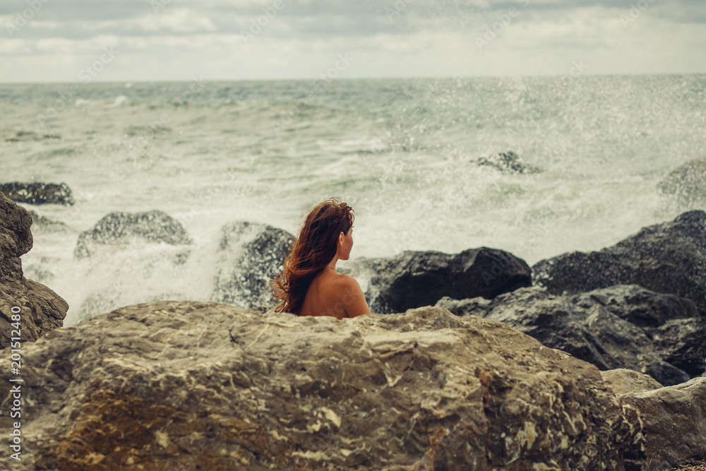 A naked young girl on the ocean coast during a storm covered herself