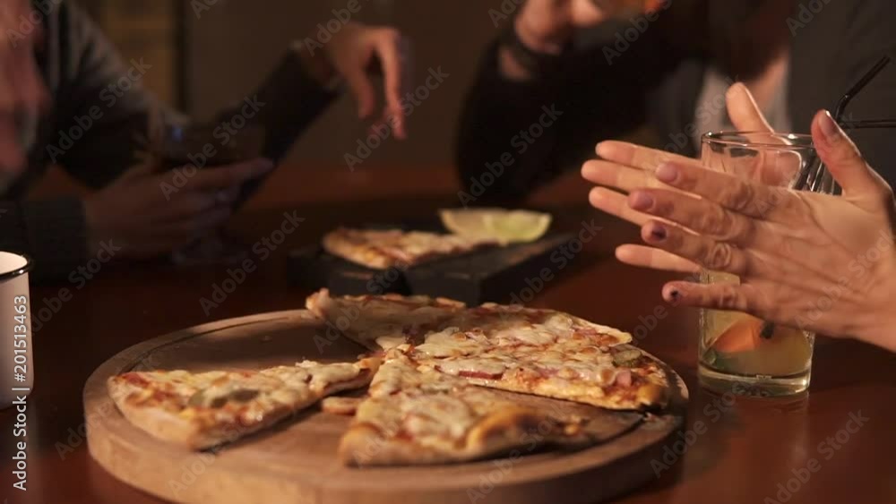 close up shot of the table on which is an appetizing pizza on a tray, glasses with alcoholic and non-alcoholic drinks, a group of people communicate in a public institution close up shot of the table on which is an appetizing pizza on a tray, glasses with alcoholic and non-alcoholic drinks, a group of people communicate in a public institution