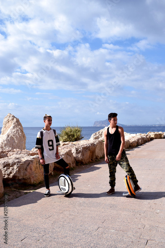 Two young guys are riding  mono wheels in the beautiful natural park  Rock of Ifach on the Mediterranean coast of Costa Blanca in Spain photo