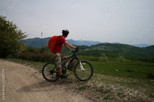 A young man on a bicycle looks at the mountains visible in the distance