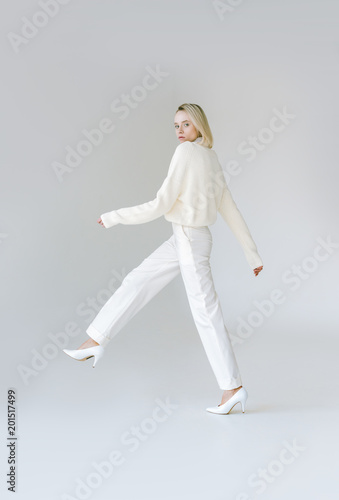 side view of attractive stylish blonde woman walking in white clothes on white