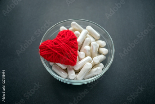 White veg capsules and red thread heart in glass bowl on black background. Anticoagulant, Blood Thinners. Cardiac Medications, pills for the heart. Treat Heart disease Failure