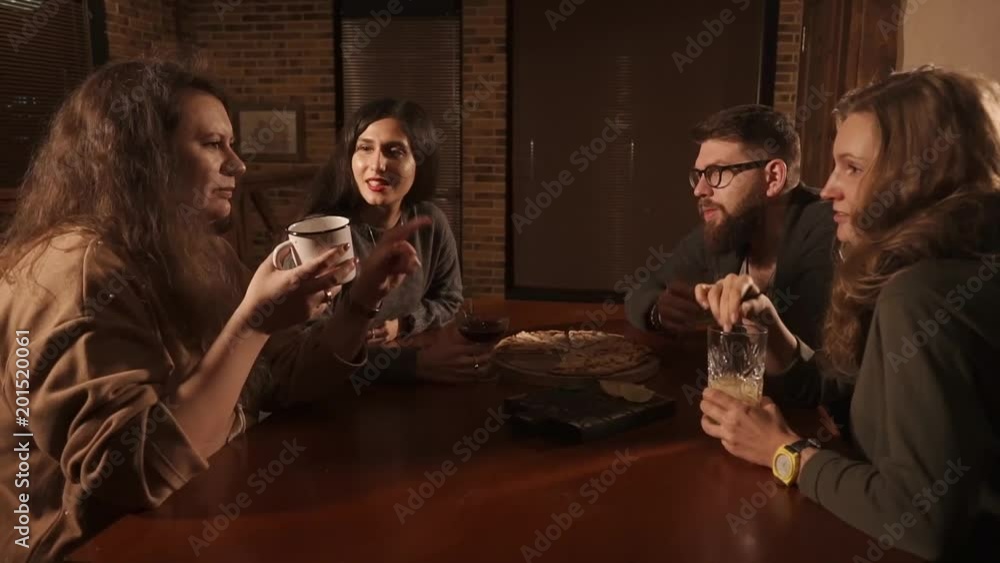 Informal meeting of colleagues in a pizzeria in evening time. People are drinking beverages telling funny stories to each other Informal meeting of colleagues in a pizzeria in evening time. People are drinking beverages telling funny stories to each other