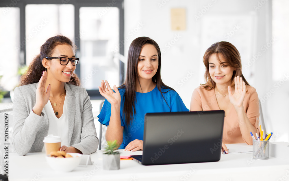 business, technology and people concept - happy smiling businesswomen having video chat by laptop computer at office business, technology and people concept - happy smiling businesswomen having video chat by laptop computer at office