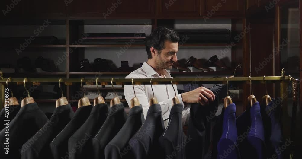 A handsome man with a white shirt, is choosing a jacket from the clothes hangers A handsome man with a white shirt, is choosing a jacket from the clothes hangers