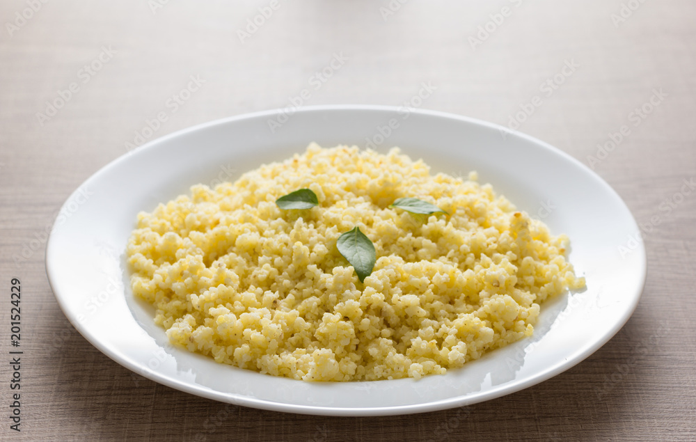 Cooked Millet cereal grain on white plate and wooden table. Detail of meal, closeup, selective focus. Cooked Millet cereal grain on white plate and wooden table. Detail of meal, closeup, selective focus.