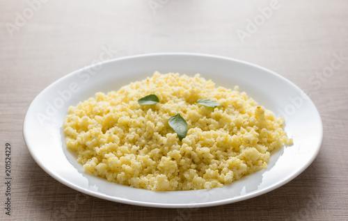 Cooked Millet cereal grain on white plate and wooden table. Detail of meal, closeup, selective focus.