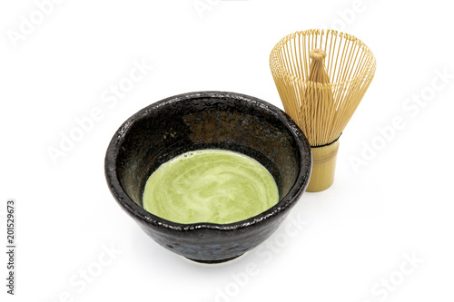 Organic matcha green tea in a Japanese ceramic tea cup with a bamboo tea whisk on white background