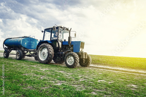 tractor of blue color with a barrel trailer rides along the spring field along the road