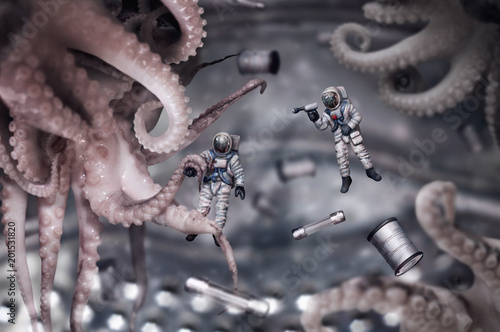 Conceptual photo of two toy astronauts fighting with alien octopuses in zero gravity.