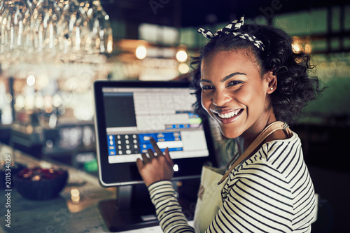 Quadro em tela Smiling African waitress using a restaurant point of sale termin