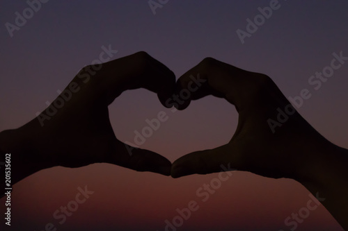 Silhouette heart shape by hand extremely underexposed with sunset background