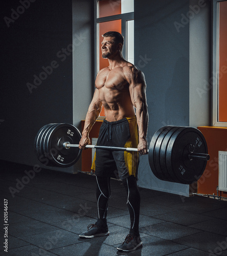 european caucasian athletic man doing deadlift with heavy barbell. man lifting barbell opposite window. emotional moment of lifting weight. affective lifting in gym. posing in gym