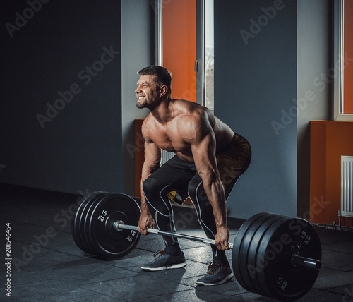 european caucasian athletic man doing deadlift with heavy barbell. man lifting barbell opposite window. emotional moment of lifting weight. affective lifting in gym. posing in gym