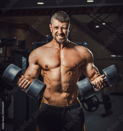 european caucasian athletic man bodybuilder holding dumbell and showing his muscular arms. man doing exercise for biceps. Biceps workout clouse-up. at once two dumbbells © Oleksandr