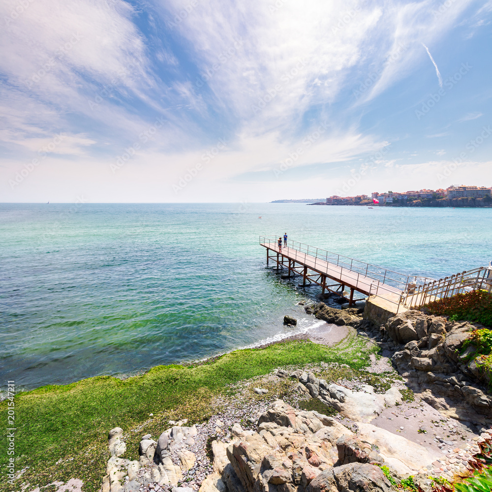 pierce on the seashore in summer. beautiful weather. people in the distance have a photo shoot. Nice travel location of Sozopol, Bulgaria pierce on the seashore in summer. beautiful weather. people in the distance have a photo shoot. Nice travel location of Sozopol, Bulgaria