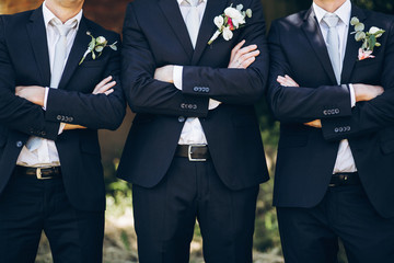 stylish groom in suit posing with groomsmen in garden on wedding day. luxury men in  rich outfits standing together. friendship