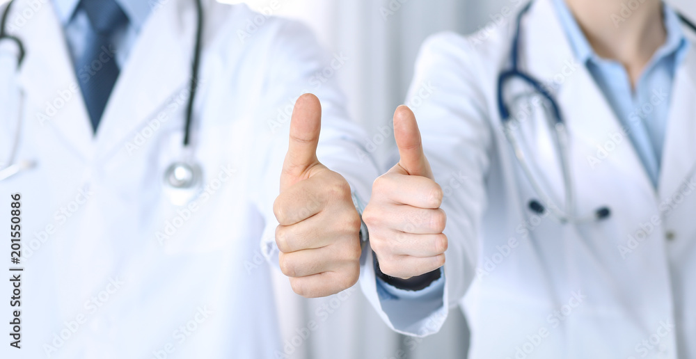 Team of unknown medicine doctors showing OK sign with thumb up close up. Success and high level service in health care, best treatment and customer loyalty and physical concept Team of unknown medicine doctors showing OK sign with thumb up close up. Success and high level service in health care, best treatment and customer loyalty and physical concept