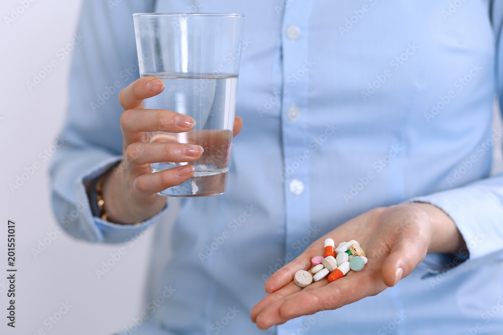 Young unknown woman holding pills and glass of water, closeup of hands. Medicine and healthcare concept Young unknown woman holding pills and glass of water, closeup of hands. Medicine and healthcare concept