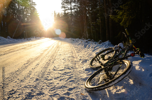 Mountain bicycle on the snowy road in winter forest at sunset