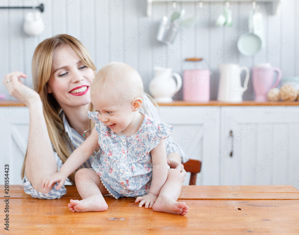 Young mother playing with her baby daughter in a modern kitchen setting. so cute family. Funny girl with mom on kitchen. Young mother playing with her baby daughter in a modern kitchen setting. so cute family. Funny girl with mom on kitchen.