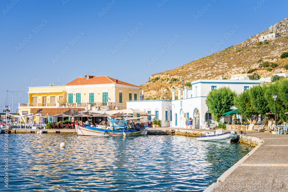 Obraz premium Beautiful sunny greek village town harbor view to the aegean blue sea with crystal clear water boats cruising surrounded by hills mountains windmills, Agia Marina, Leros Island, Dodecanese, Greece