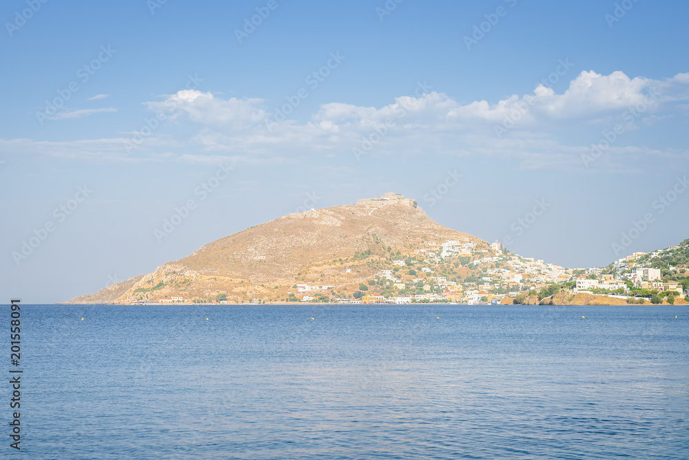 Leros Island, Dodecanese, Greece: Beautiful sunny coast view to the greek blue sea with crystal clear water beach with some boats fishing cruising surrounded by hills mountains Lakki