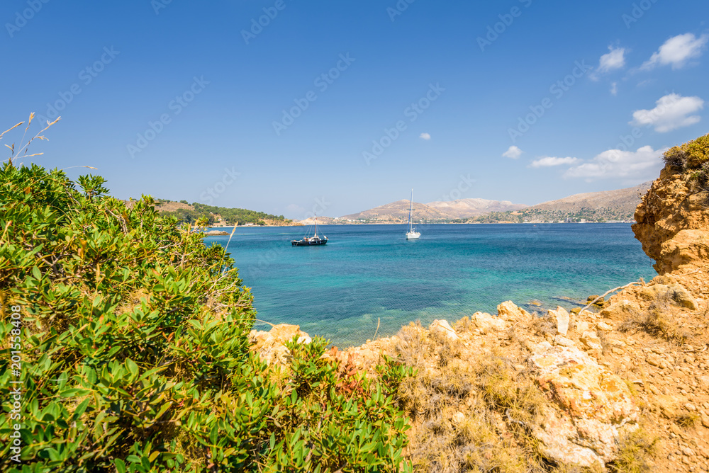 Beautiful sunny coast view to the greek blue sea with crystal clear water beach with some boats fishing cruising surrounded by hills, Kokkina Beach, Leros, Dodecanese Islands/ Greece – July 18 2017 Beautiful sunny coast view to the greek blue sea with crystal clear water beach with some boats fishing cruising surrounded by hills, Kokkina Beach, Leros, Dodecanese Islands/ Greece – July 18 2017