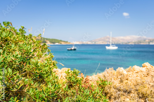 Beautiful sunny coast view to the greek blue sea with crystal clear water beach with some boats fishing cruising surrounded by hills, Kokkina Beach, Leros, Dodecanese Islands/ Greece – July 18 2017