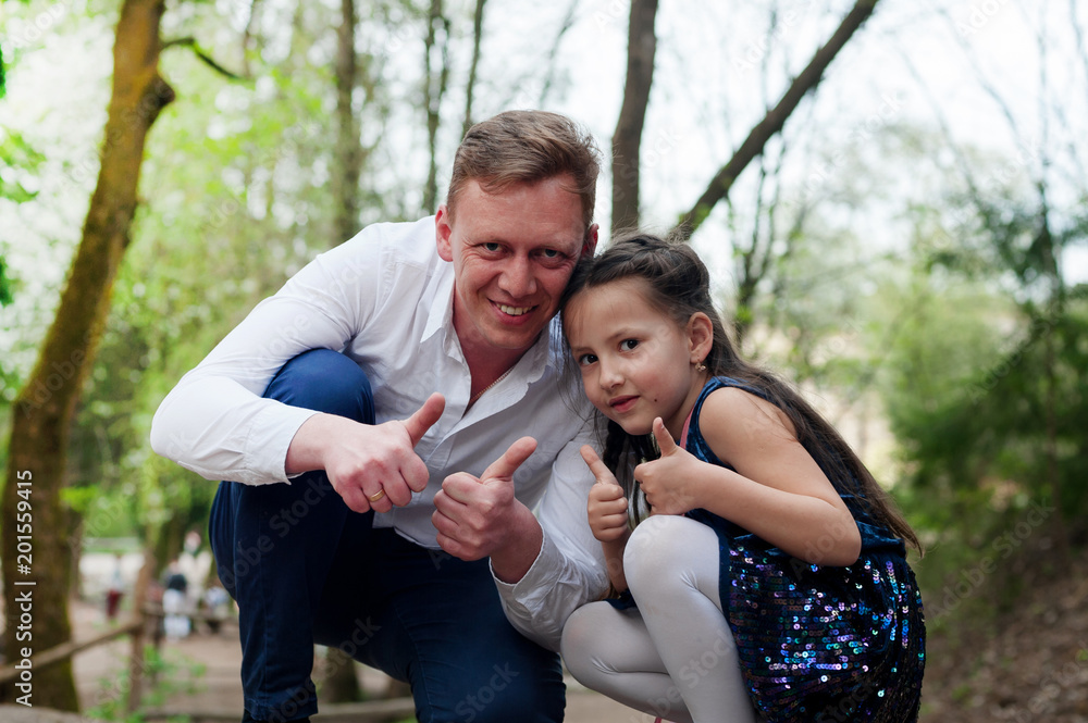 Happy father and daughter in the park sat down on the roadside. Shoot your finger up Happy father and daughter in the park sat down on the roadside. Shoot your finger up