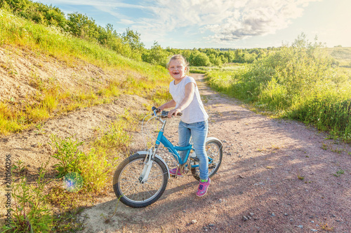 Happy child riding bike. Young girl on bicycle in sunny summer park. Healthy school children summer activity. Kids playing and cycling outdoors. Little girl learns to keep balance while riding bicycle