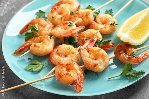 Plate with delicious fried shrimp skewers and lemon on grey background, closeup