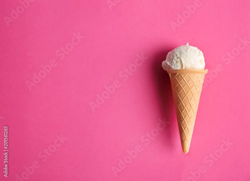 Waffle cone with tasty vanilla ice cream on color background