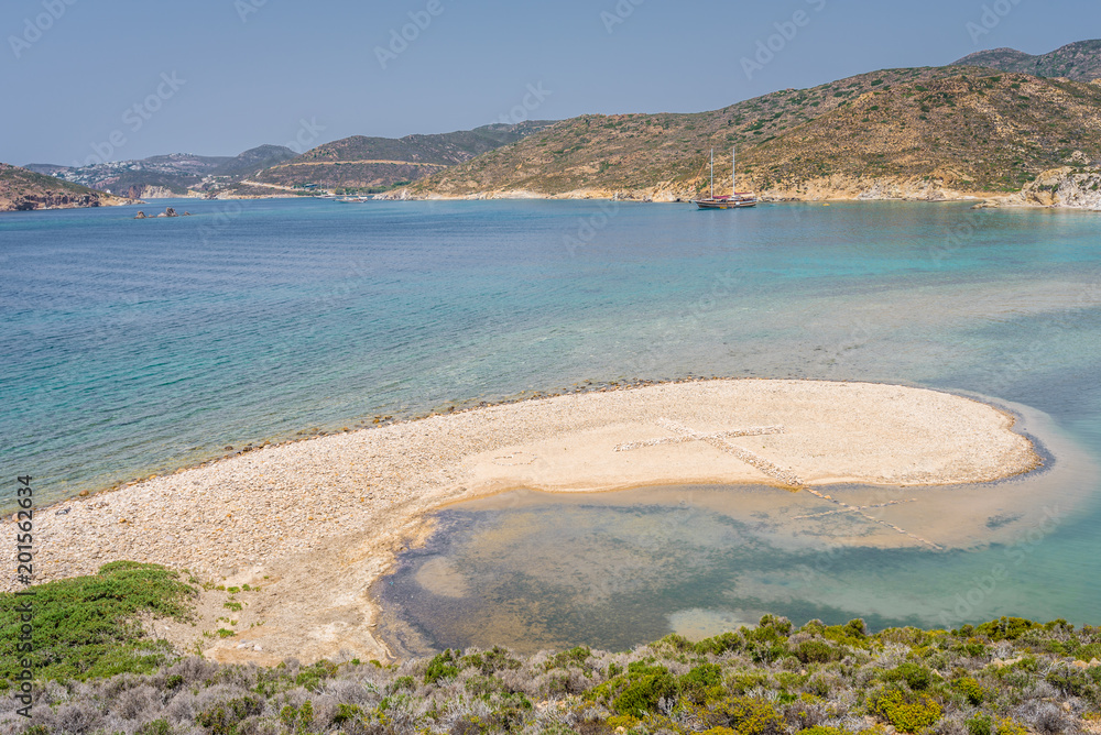 Peaceful sunny coast view to a empty greek holiday bay with crystal clear blue water sandy beach for sunbathing and some boats cruising fishing in background