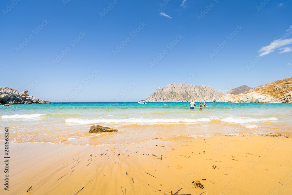 Beautiful sunny coast view to a cozy holiday bay with crystal clear blue water sandy beach for sunbathing and some boats cruising fishing in background, Patmos Island, Dodecanese/ Greece - 07 27 2017