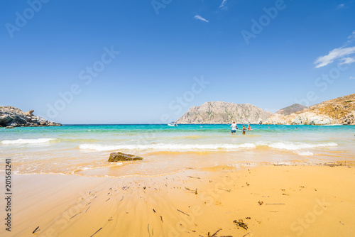 Beautiful sunny coast view to a cozy holiday bay with crystal clear blue water sandy beach for sunbathing and some boats cruising fishing in background  Patmos Island  Dodecanese  Greece - 07 27 2017