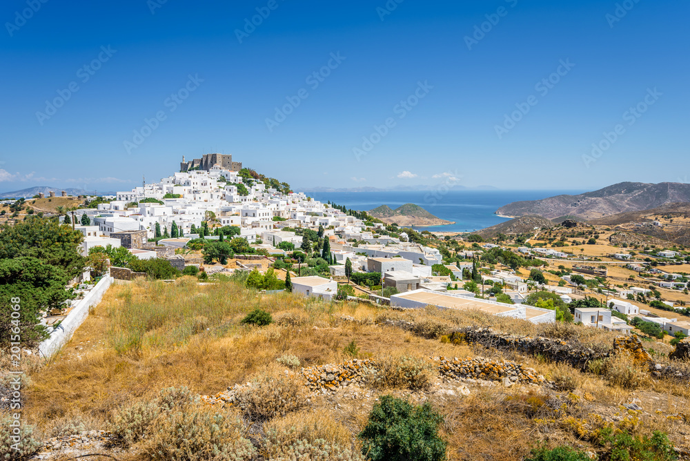 Amazing sunny view from old monastery castle Chora a small greek town near Skala with harbour and blue sea with crystal clear water surrounded by hills mountains, Patmos Island, Dodecanese, Greece