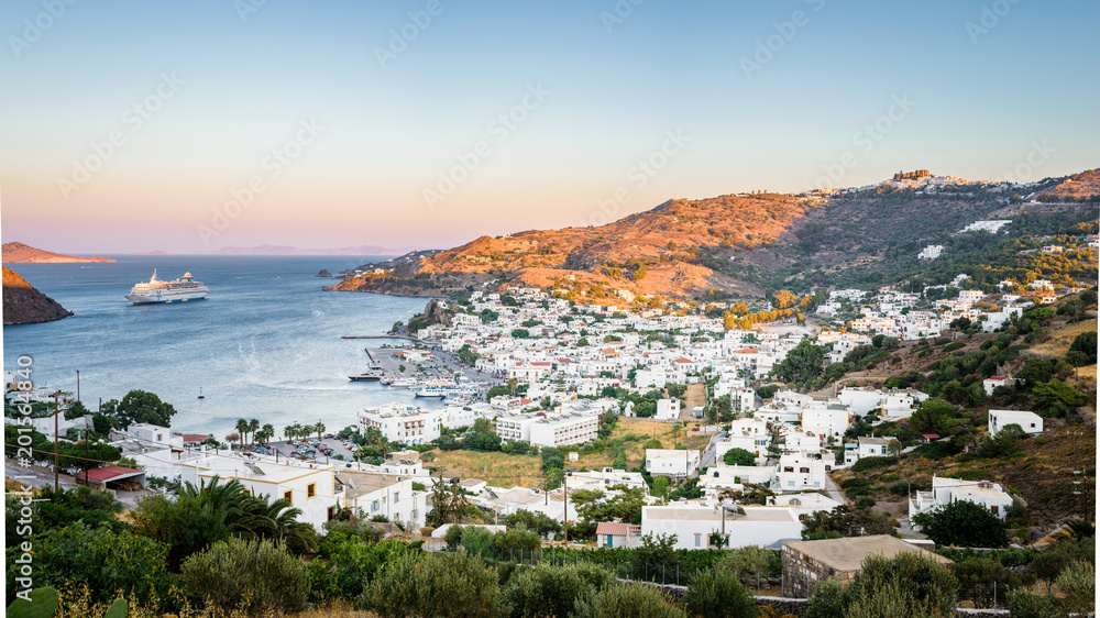 Skala, Patmos Island, Dodecanese, Greece: Beautiful sunny sunset greek village town harbor view white church to the aegean sea with crystal clear water surrounded by mountains and ferry in background