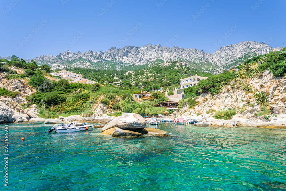 Beautiful sunny greek village town church and harbor view to the blue sea with crystal clear water and fishing boats cruising yacht at shore, Ikaria Island, Magganitis, Sporades/ Greece – 08 01 2017