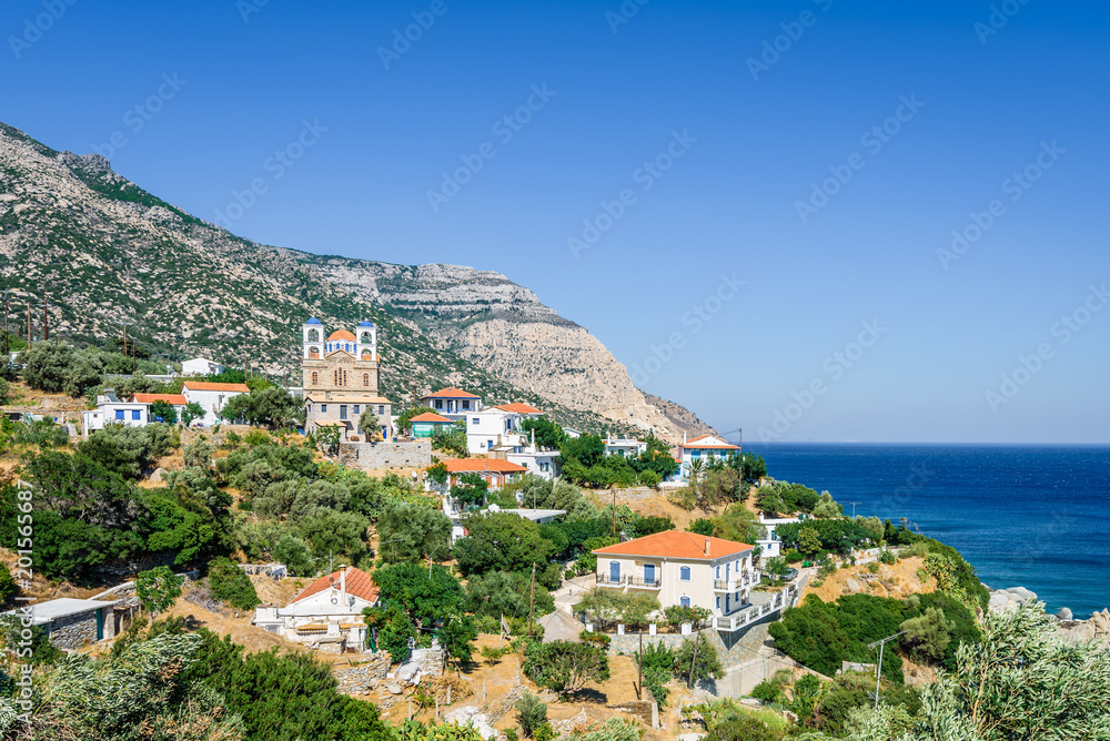 Beautiful sunny greek village town church and harbor view to the blue sea with crystal clear water and fishing boats cruising yacht at shore, Ikaria Island, Magganitis, Sporades/ Greece – 08 01 2017