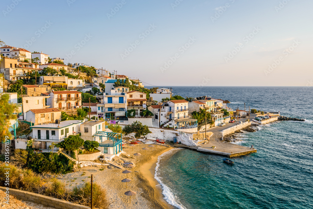 Relaxing at the greek mediterranean sea and enjoyng a warm sunset over a blue sky with a few clouds over the horizon and the small traditional village called Armenistis, Ikaria, Sporades, Greece