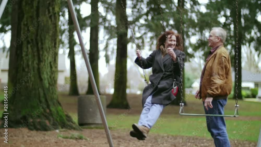 Elderly loving couple playing on a swing at a park Elderly loving couple playing on a swing at a park