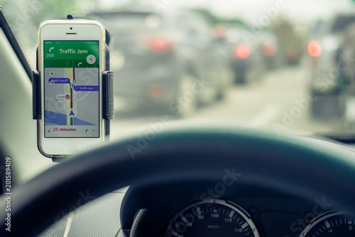 Mobile phones show traffic jam map. View from the inside of the car through the steering wheel to the cell phone, open GPS application. Background is traffic jams in the city. Shallow depth of field. 