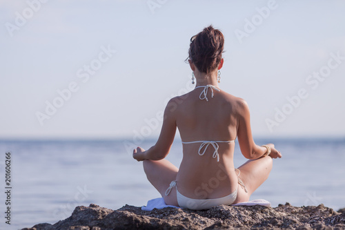 Girl in white bikini sits on rock