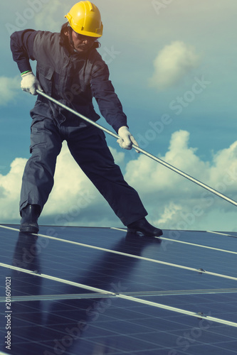 technician operating and cleaning solar panels at generating power of solar power plant; technician in industry uniform on level of job description at industrial