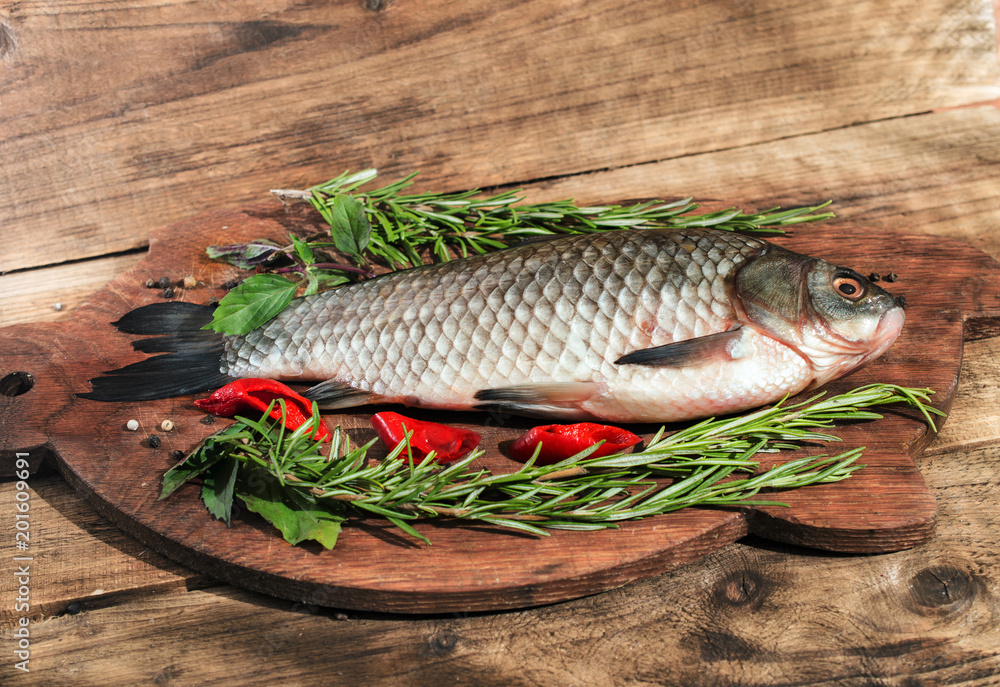 Fresh fish with herbs and pepper before cooking on wooden background Fresh fish with herbs and pepper before cooking on wooden background